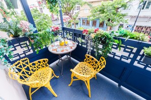 Ein Balkon mit zwei gelben Stühlen, einem kleinen runden Tisch mit Getränken und Blumentöpfen.