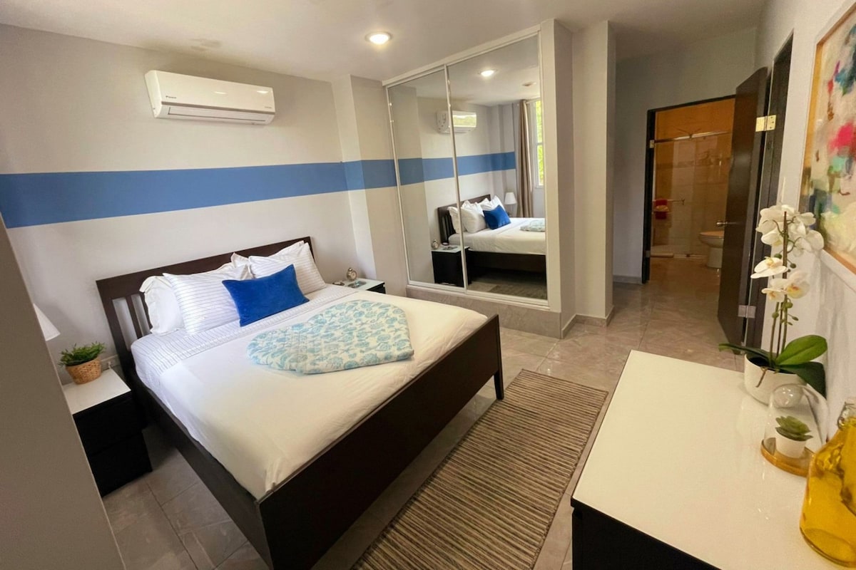 Ein Hotelzimmer mit Bett, Nachttisch, Spiegel und einem durch eine Glastür einsehbaren Badezimmer.