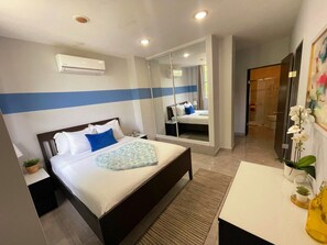 Ein Hotelzimmer mit Bett, Nachttisch, Spiegel und einem durch eine Glastür einsehbaren Badezimmer.