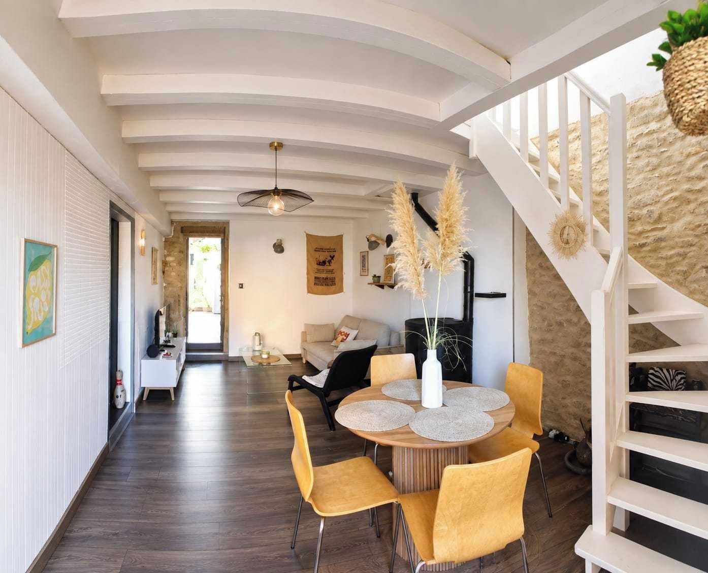 Un interno moderno con zona pranzo, un tavolo rotondo e sedie gialle, una scala con ringhiera bianca e un muro in pietra.