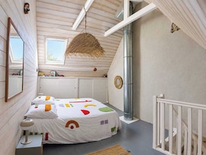 A bedroom with a bed, a hanging light fixture, a window, a radiator, and a white railing. - Charming house in the heart of the salt marshes (Guérande)