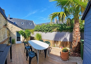 A wooden deck with a table and chairs, surrounded by a stone wall with climbing plants. - Charming house in the heart of the salt marshes (Guérande)
