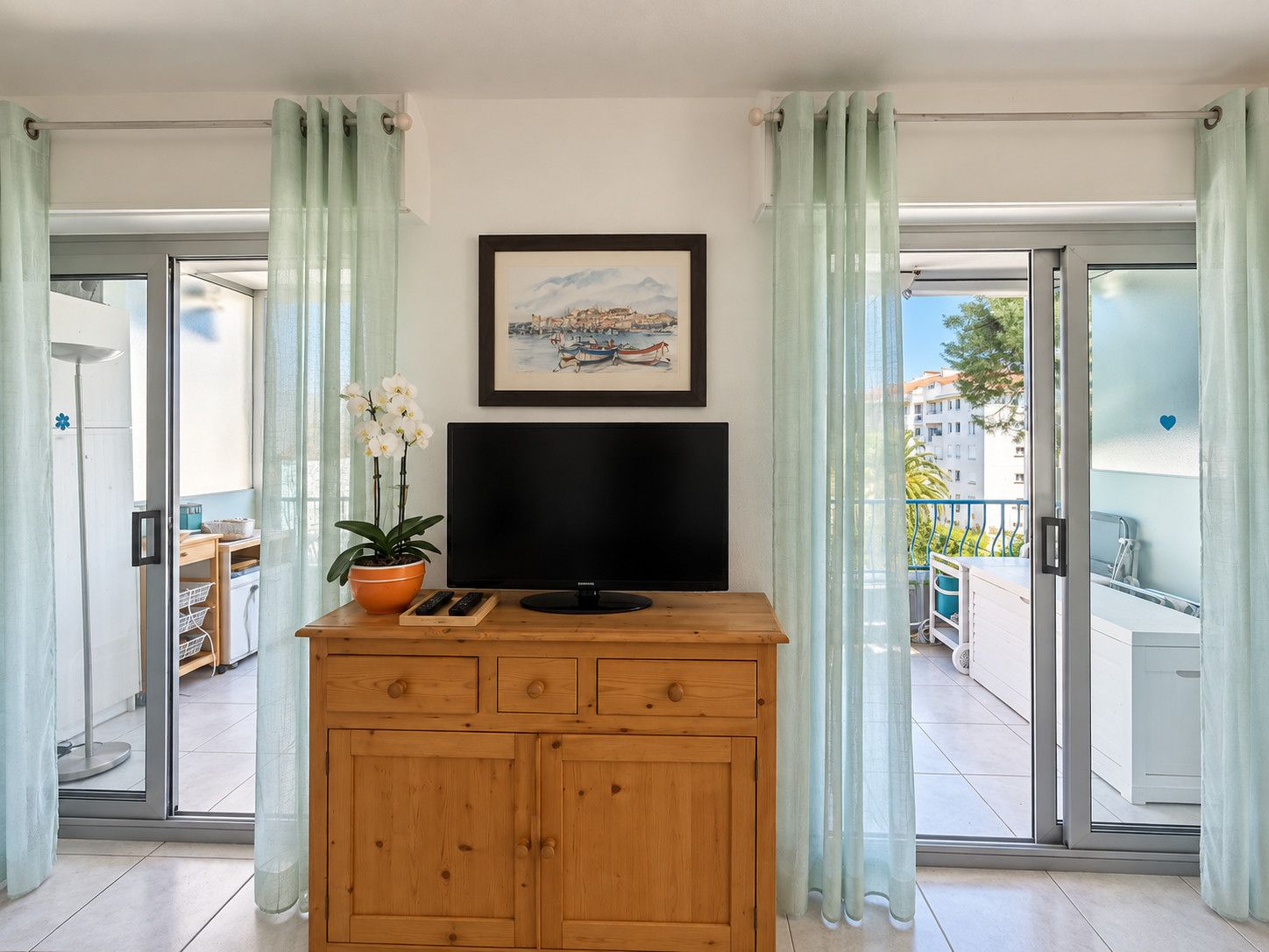 Ein Zimmer mit Fernseher auf einer Holzkommode, einer Topf-Orchidee und einem gerahmten Bild an der Wand.
