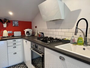 A modern kitchen with a gas stove, a built-in oven, a sink, and a red accent wall. - 2-bedroom apartment in the heart of Trouville (Trouville-sur-Mer)