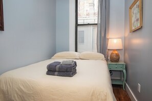 Un lit bien fait, avec une serviette pliée, une lampe de chevet et une fenêtre avec des rideaux.