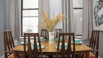 A dining table with chairs, a vase with dried plants, and a painting on the wall.