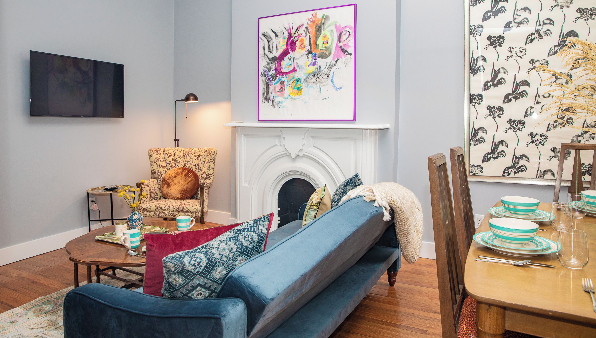 A living room with a sofa, armchair, fireplace, and dining table set with plates and glasses.