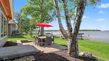 A patio with outdoor furniture and a red umbrella, overlooking a lake.