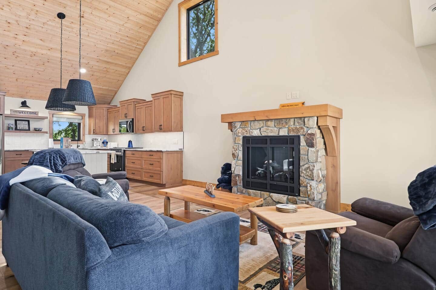 A loft-style living space with a kitchen, a stone fireplace, and a high ceiling with wooden beams.
