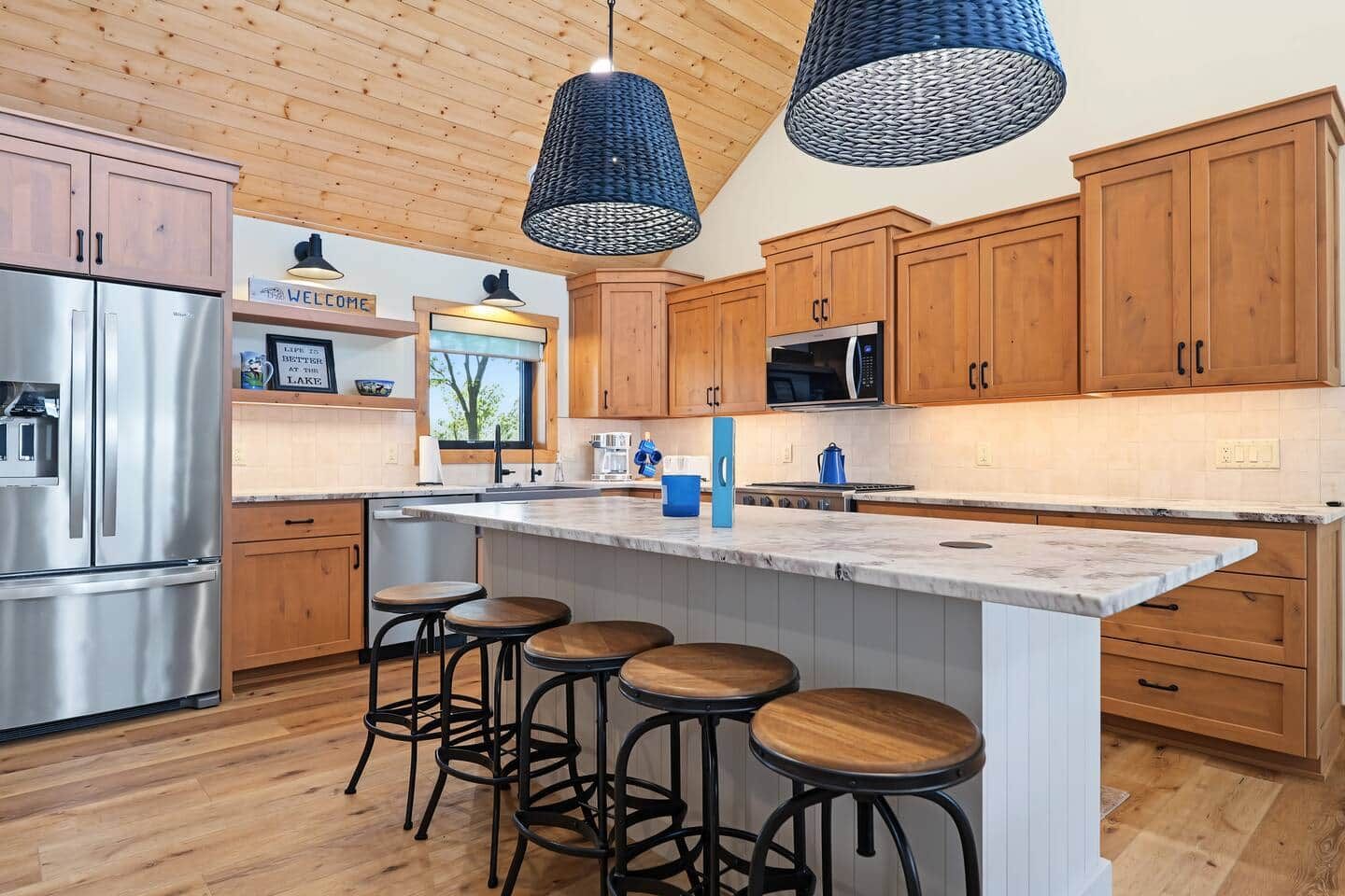 Una cucina moderna con mobili in legno, elettrodomestici in acciaio inossidabile, un'isola in marmo e sgabelli da bar.