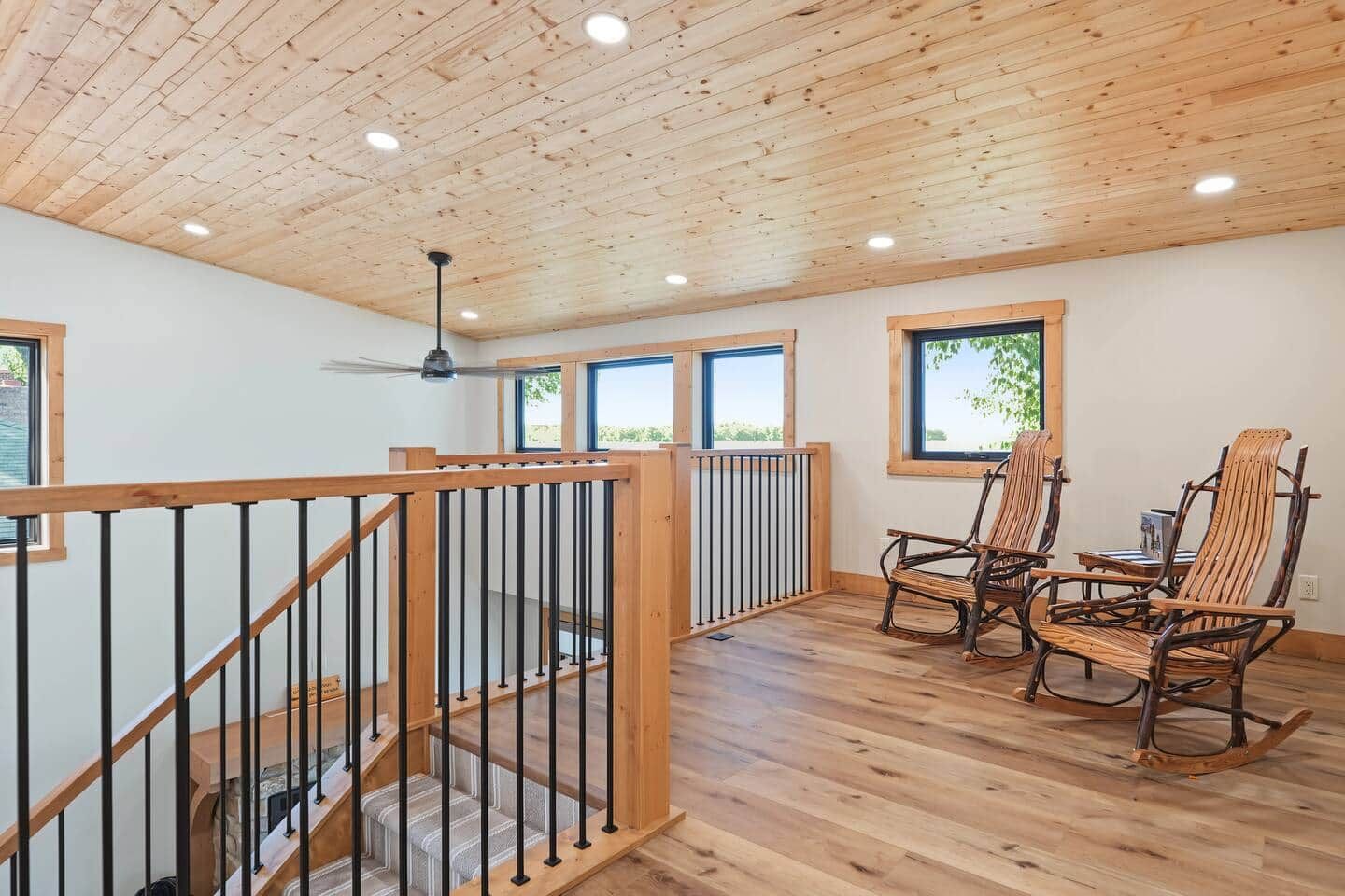 A spacious room with a wooden ceiling, a staircase with a railing, and two rocking chairs.