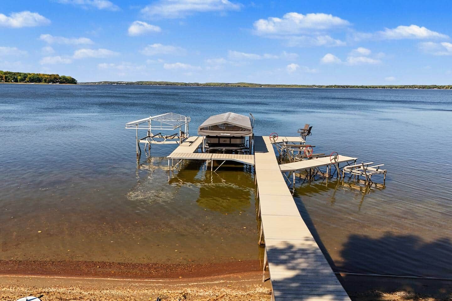 A dock extending into a calm lake with a covered structure and seating area.