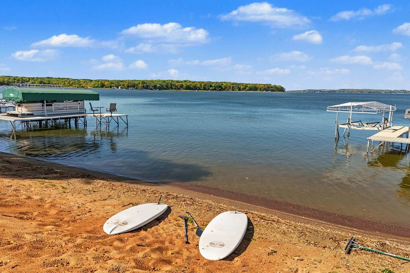 A beach with two white surfboards, a covered seating area, and a dock extending into calm water.