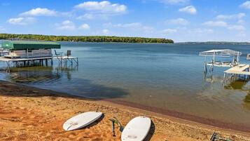 A beach with two white surfboards, a covered seating area, and a dock extending into calm water.