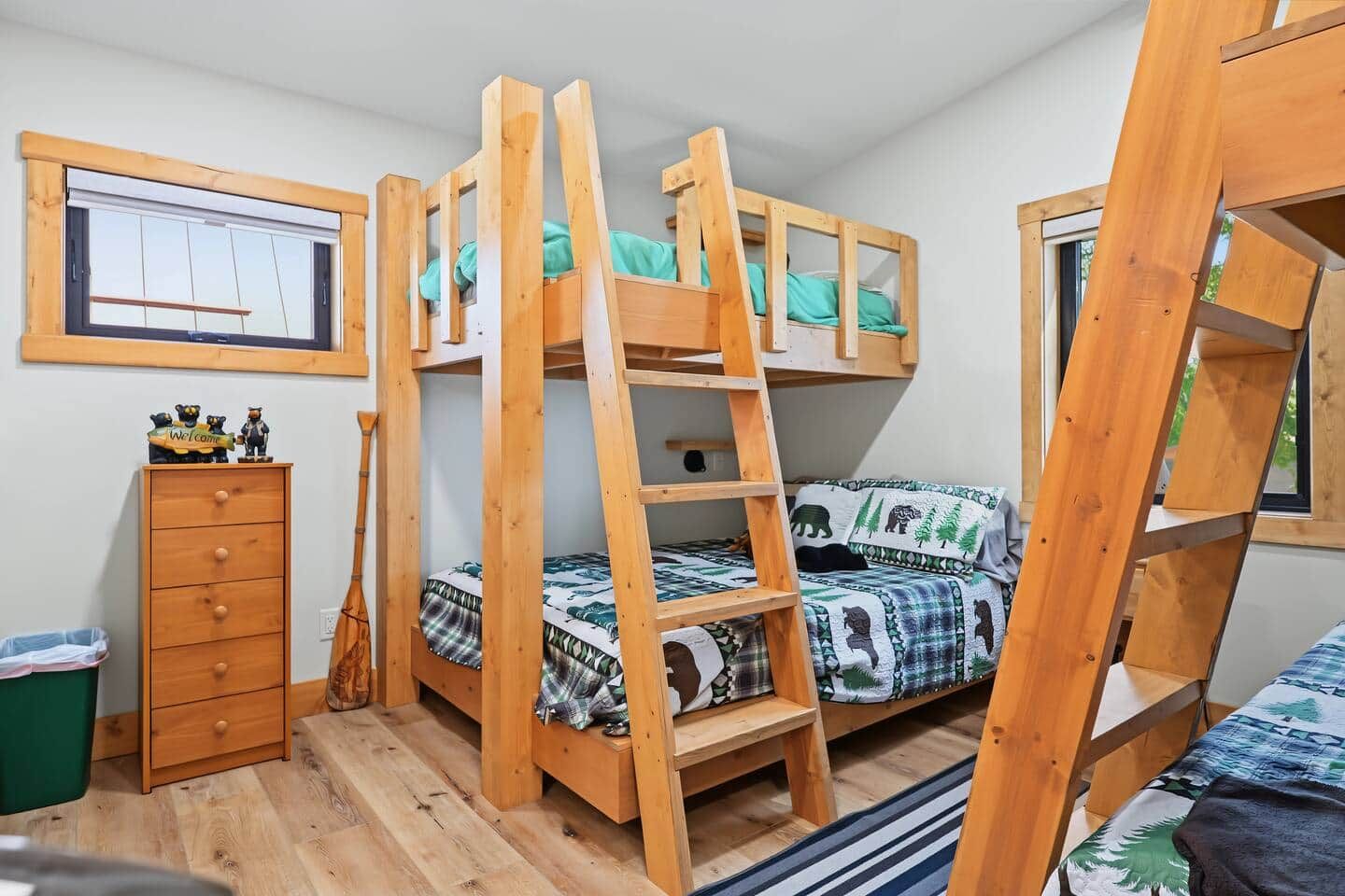A bunk bed room with a ladder, a wooden dresser, and a window.