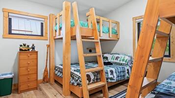 A bunk bed room with a ladder, a wooden dresser, and a window.