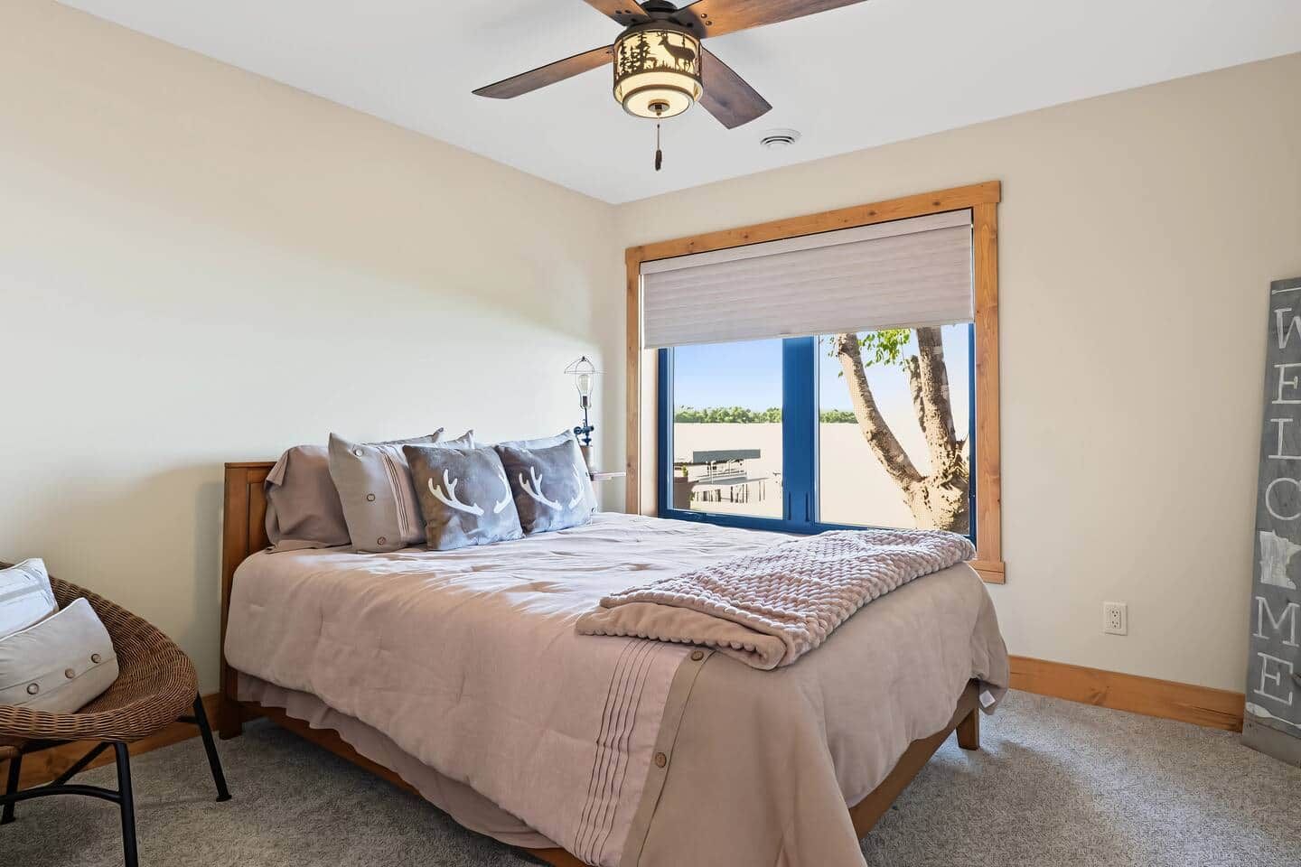 A bedroom with a bed, a ceiling fan, a window with a view, and a welcome sign.