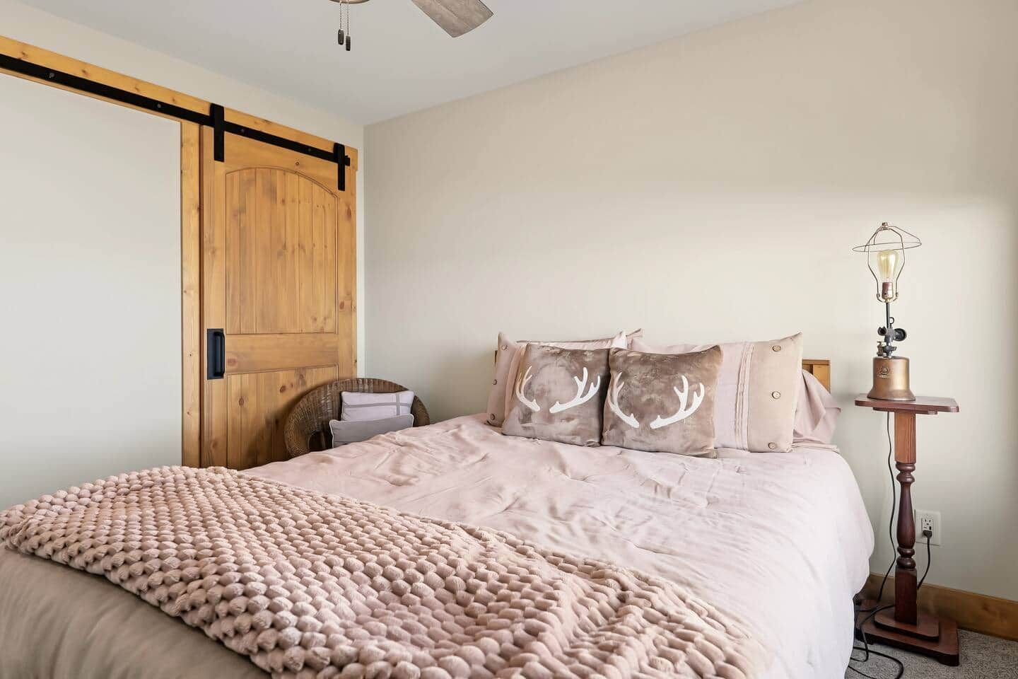 A bedroom with a bed, a wooden wardrobe, a wicker chair, and a floor lamp.