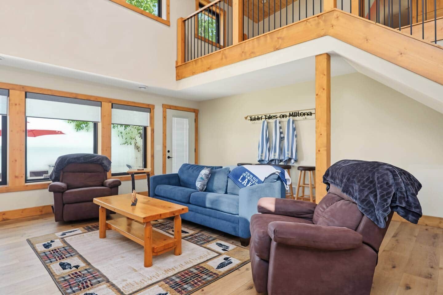 A spacious living area with a high ceiling, wooden beams, a blue sofa, two armchairs, a wooden coffee table, and a patterned rug.