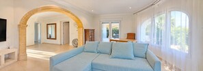 A spacious living room with a light blue sofa, a wooden cabinet, and a large arched doorway leading to another room. - Villa 'Vera' with sea view, Wi-Fi, heated pool and air conditioning (Balcó al Mar)