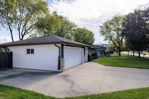 A single-story residential garage with a sloped roof, adjacent to a house with a garage door. - Walking distance to Lambeau Field- Dog Friendly! (Green Bay)