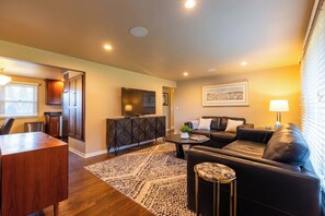 A modern living room with a sofa, coffee table, and a TV. There is a dining area with a table and chairs. The room has wooden flooring and a patterned rug. - Walking distance to Lambeau Field- Dog Friendly! (Green Bay)