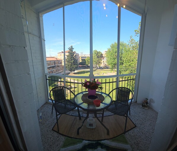 A covered balcony with two chairs and a table, a potted plant, and a view of buildings and trees. - La Dimora Di Mari—10 minutes from Sassi—easy parking—Wi-Fi (Matera)