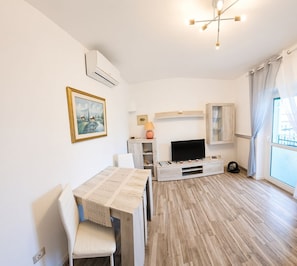A modern living room with a dining area, a flat-screen TV, and a large window with curtains. - La Dimora Di Mari—10 minutes from Sassi—easy parking—Wi-Fi (Matera)