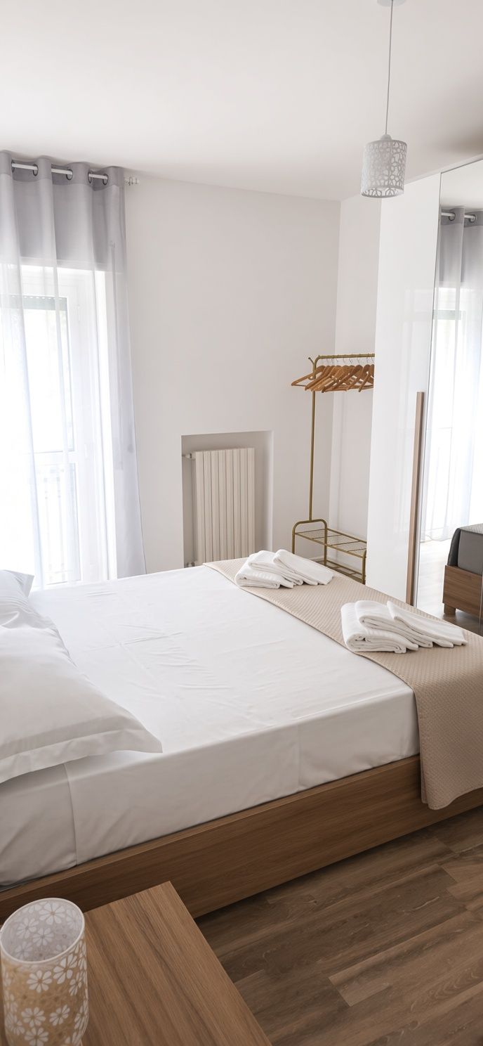 A hotel room with a bed, a bedside table with a lamp, a radiator, and a window with curtains.