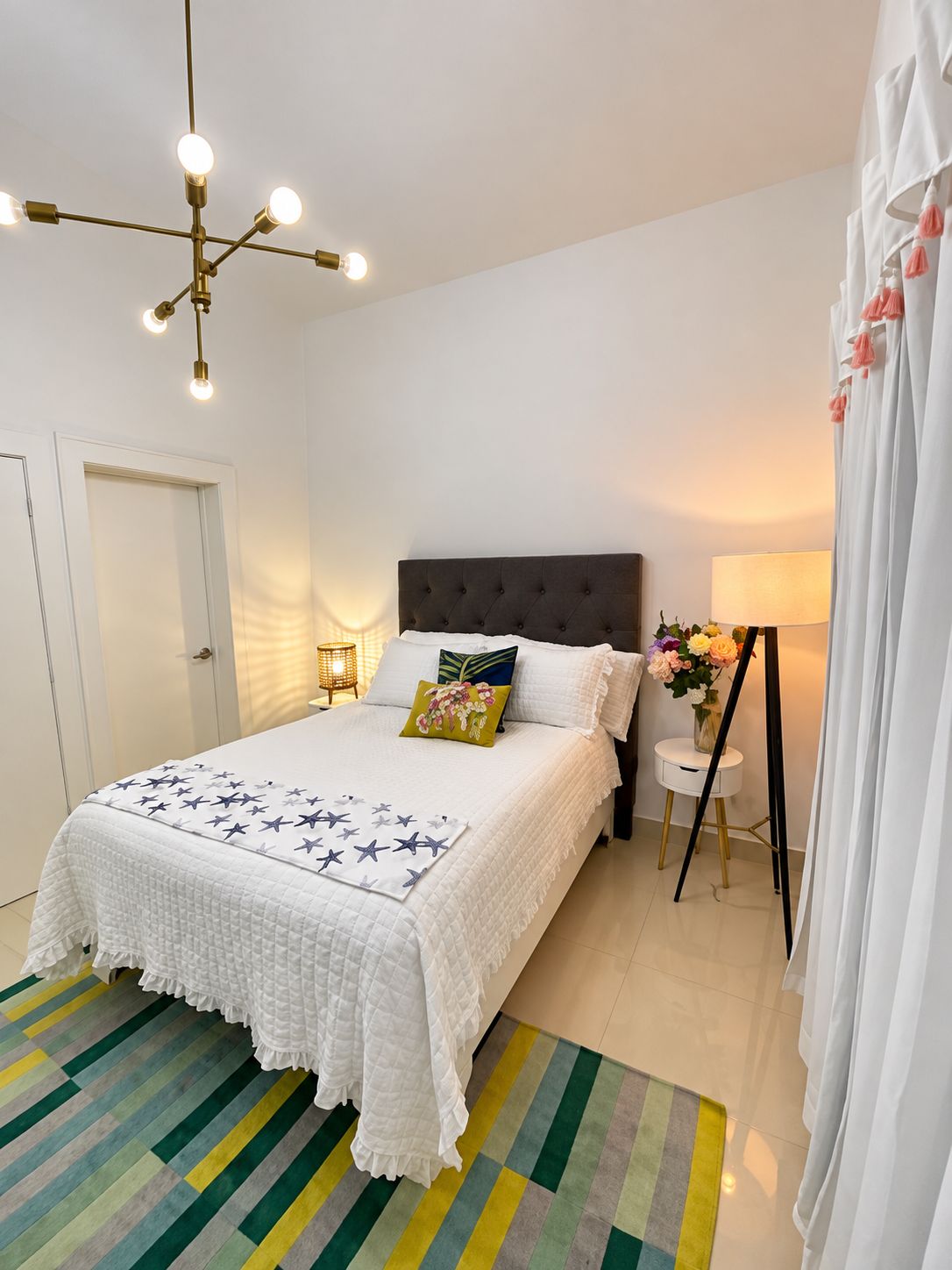 A bedroom with a bed, bedside lamps, a nightstand, a chair, and a wall-mounted lamp.