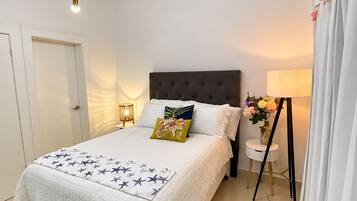 A bedroom with a bed, bedside lamps, a nightstand, a chair, and a wall-mounted lamp.