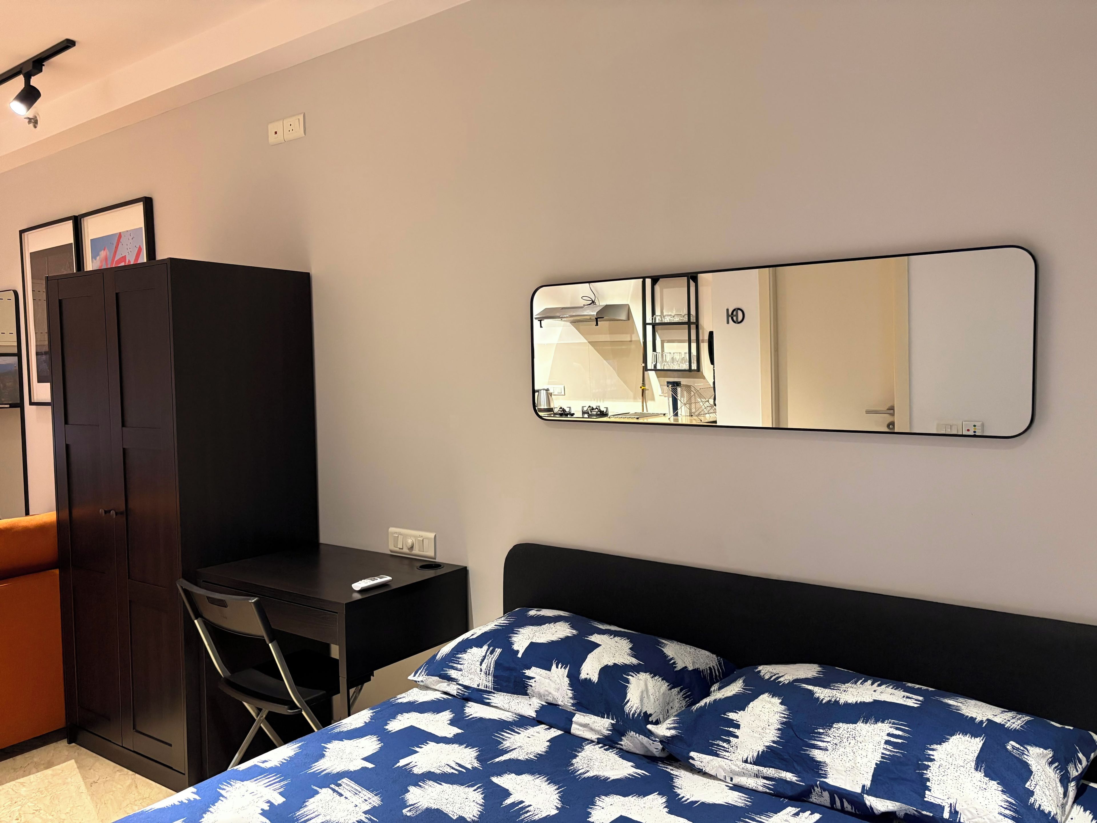 Un dormitorio con cama, escritorio, silla, armario y espejo en la pared.