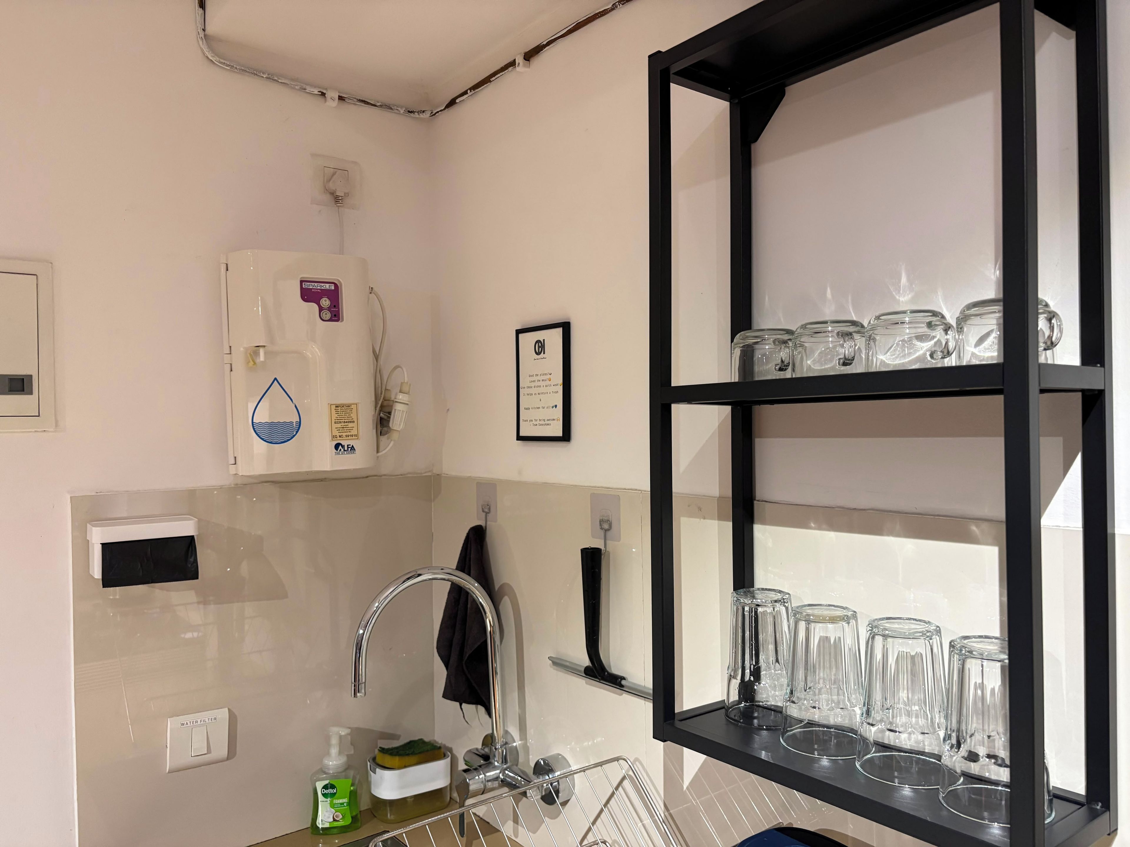 Una cocina con dispensador de agua, un lavamanos y una estantería con cristalería.