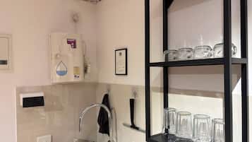 Una cocina con dispensador de agua, un lavamanos y una estantería con cristalería.