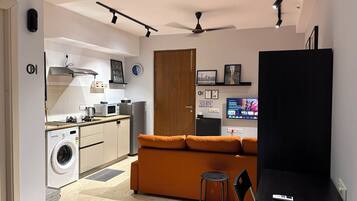 A compact living space with a kitchenette, a sofa, a television, and a ceiling fan.