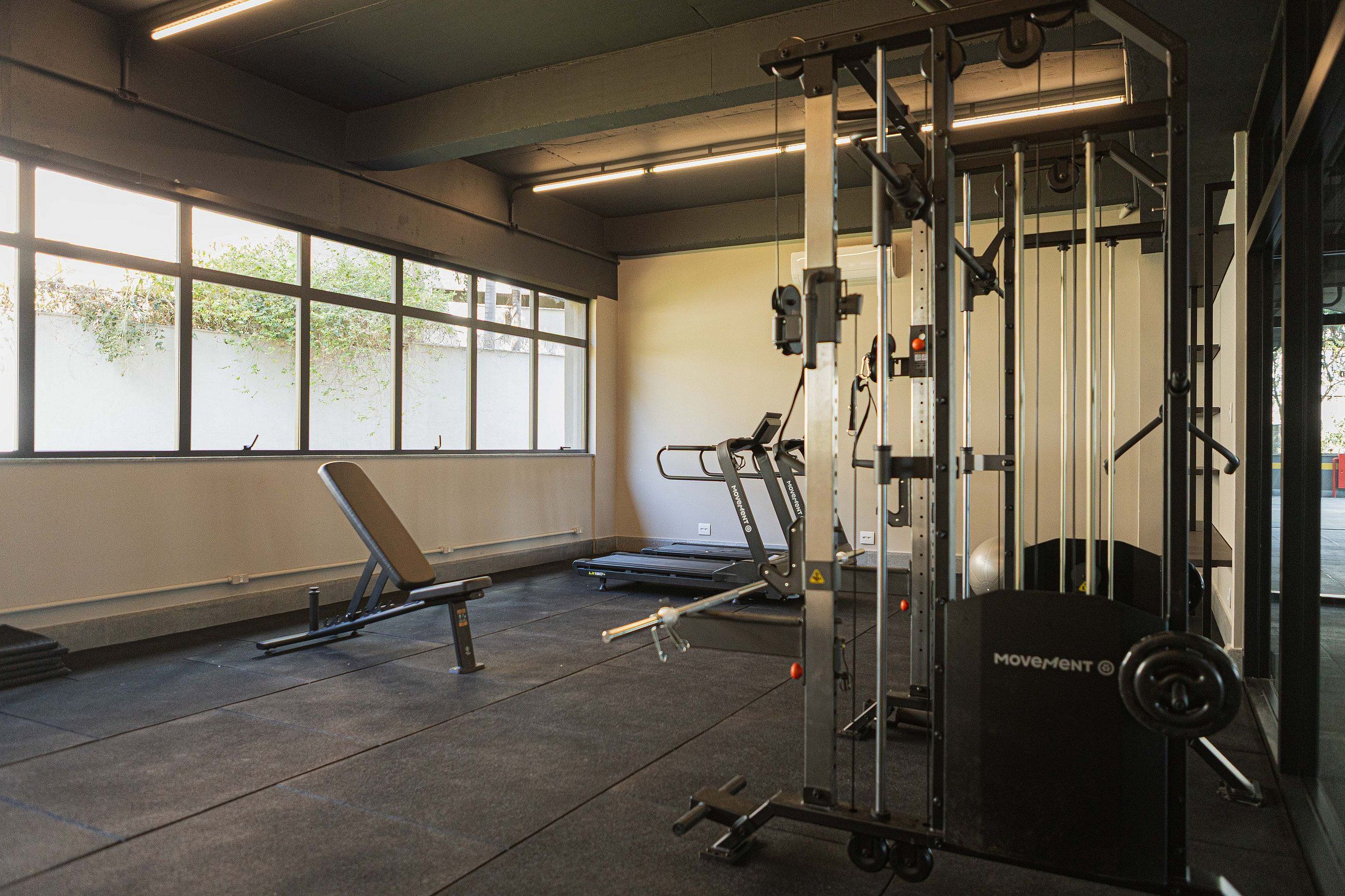 Une salle de sport équipée de matériel d’exercice, d’un banc et de grandes fenêtres.