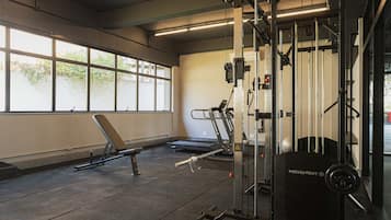 Une salle de sport équipée de matériel d’exercice, d’un banc et de grandes fenêtres.