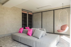 A modern living room with a grey sofa, pink cushions, a hanging chair, and a large window.