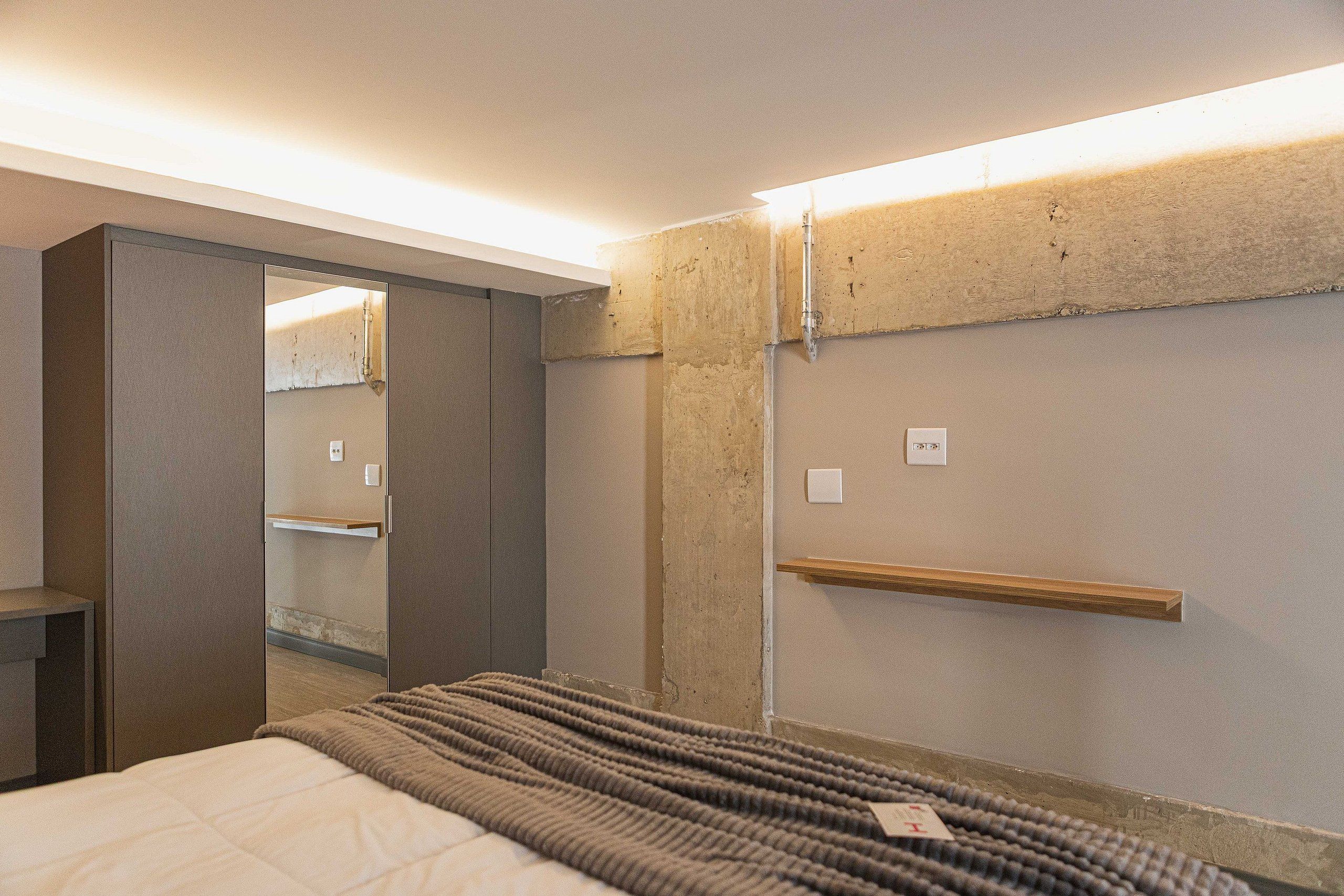 Un dormitorio con una cama, un armario, un espejo y una estantería.