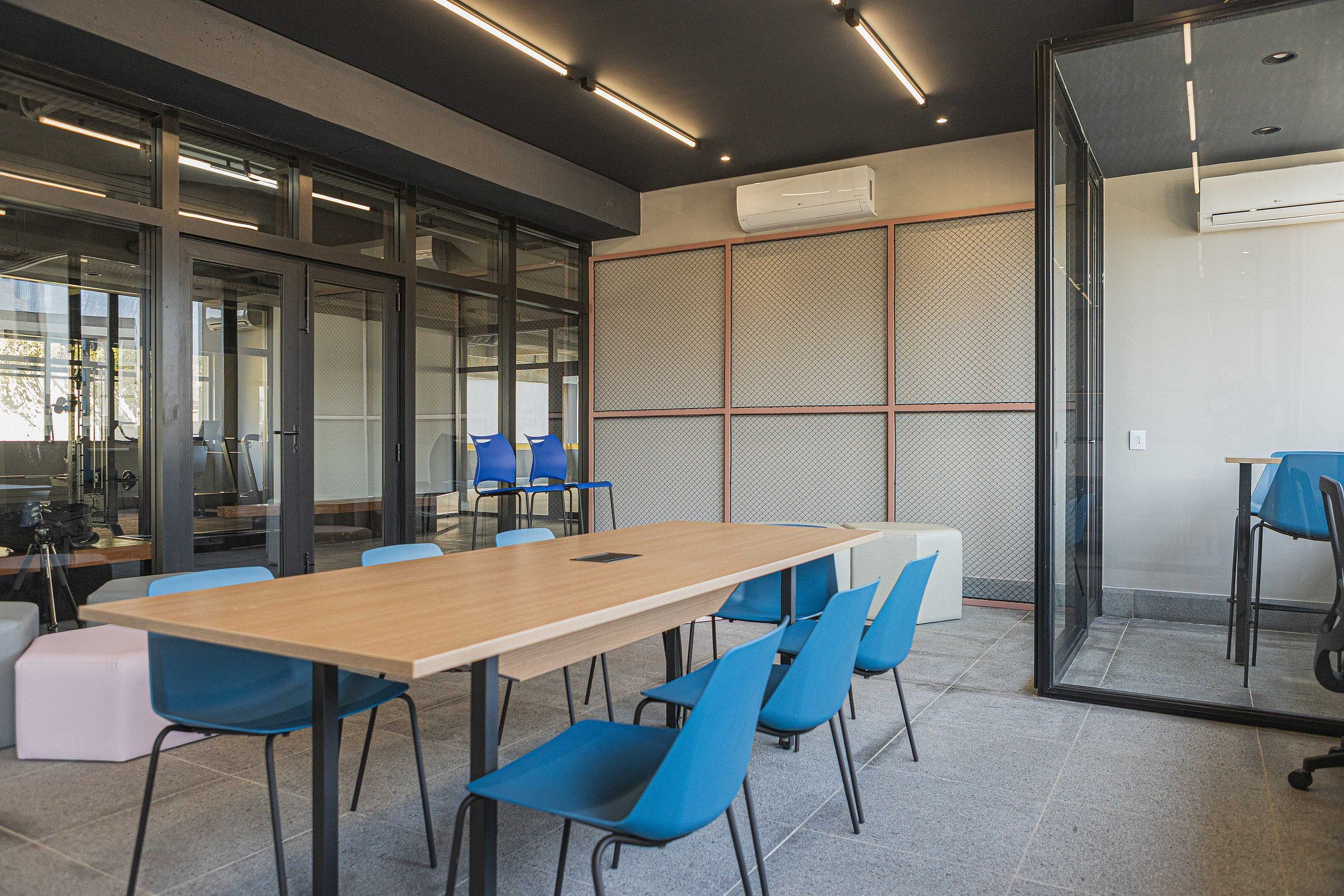 A conference room with a long table, blue chairs, and glass walls.