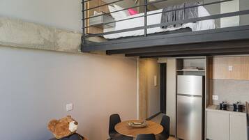 Un espacio habitable pequeño con kitchenette, una zona de comedor con mesa y sillas, y una figurita de oso.