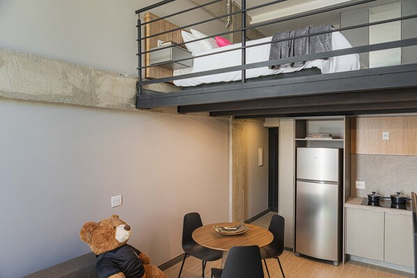 A compact living space with a kitchenette, a dining area with a table and chairs, and a bear figurine.