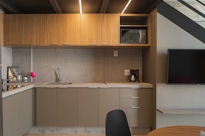 A compact kitchen with wooden cabinets, a built-in microwave, a coffee maker, and a TV mounted on the wall. - Housi Delphos (Belo Horizonte)