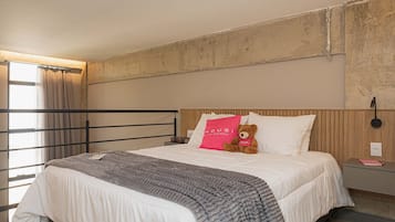 Una habitación de hotel con una cama, una mesita de noche, un oso de peluche y una ventana con cortinas.