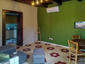 A room with a wooden ceiling, a green wall, a white air conditioner, a dining table with chairs, and a patterned floor. - Casa Cecilia (Maratea)