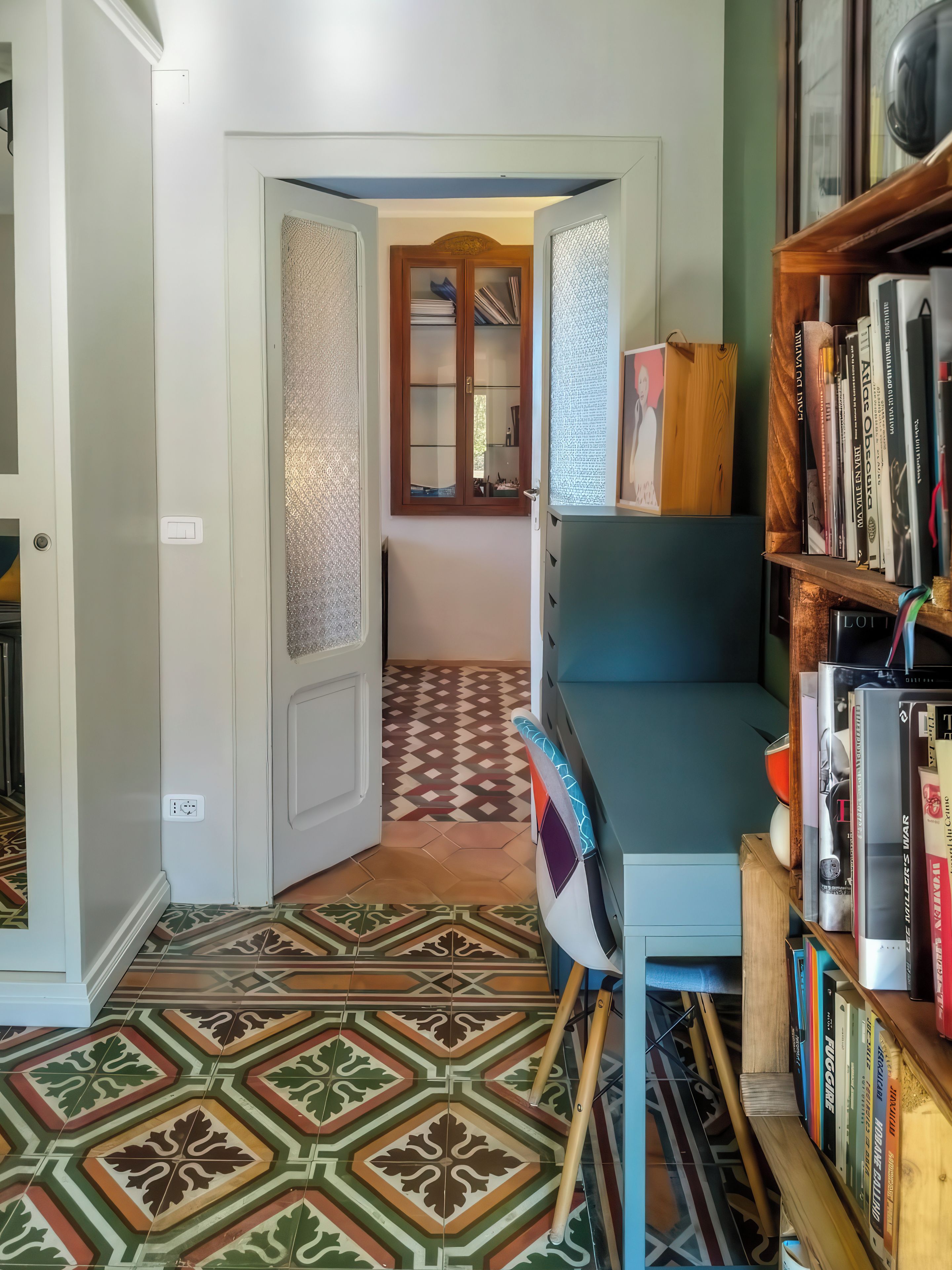 A hallway with patterned floor tiles, a bookshelf with books, and a door leading to another room.