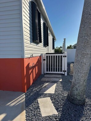 A residential property with a white exterior, a red lower section, a gated entrance, and a gravel pathway leading to the house. - Beautiful 2-bedroom, 3 bed house on canal in Saint James City. (Saint James City)