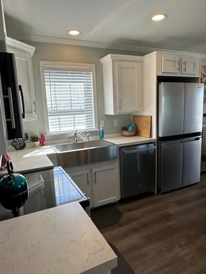 A modern kitchen with white cabinets, stainless steel appliances, and a marble countertop. - Beautiful 2-bedroom, 3 bed house on canal in Saint James City. (Saint James City)