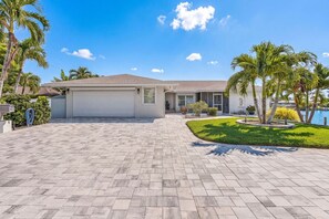 A residential property with a paved driveway, a garage, and a well-maintained lawn with palm trees. - Panoramic Water Views • Gulf Access • No Bridges (Cape Coral)