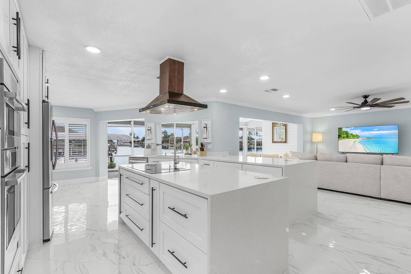 A modern kitchen with a central island, white cabinetry, and a large window overlooking a pool.
